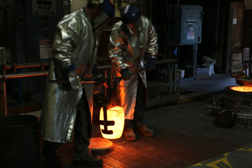 Men in heat proof suits pouring molten bronze.